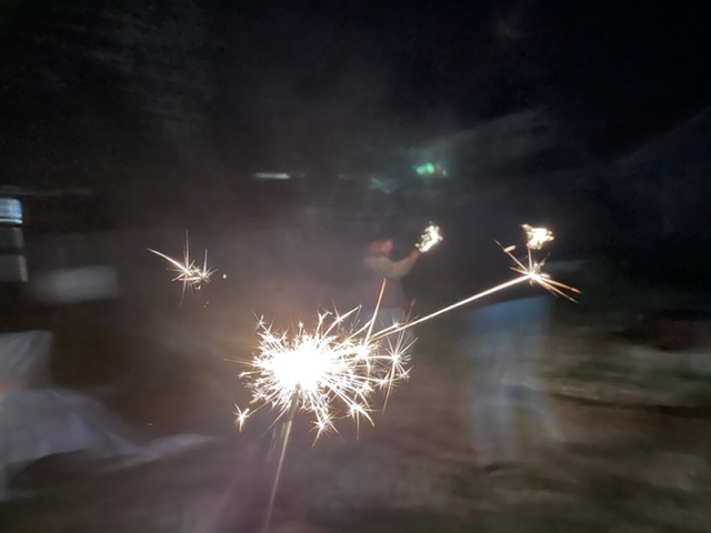 Blurry photo of people waving lit sparklers at night.