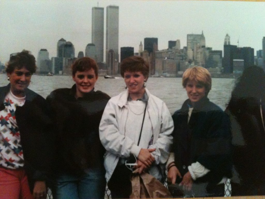 Four young, white women tourists with the Twin Towers and NY City skyline behind them, 1986.